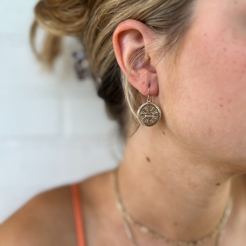 Woman Wears MIMOSA Handcrafted Sacred Heart Earrings in Bronze.