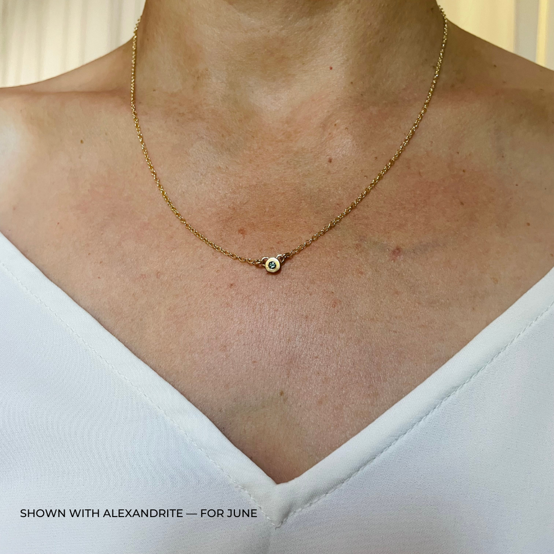 Handmade Bronze Birthstone Necklace with Alexandrite on Person Wearing a White Top