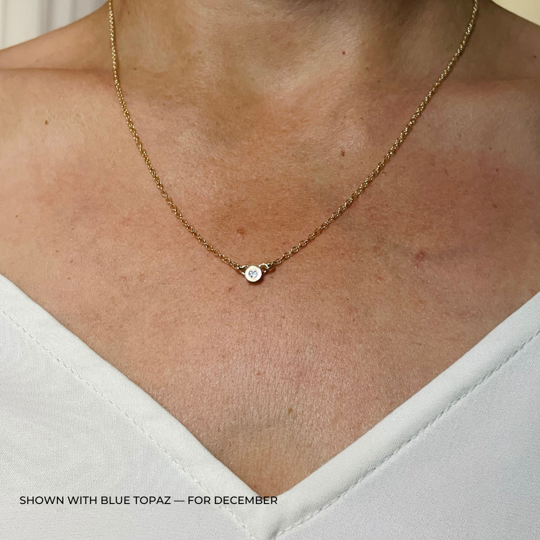 Handmade Bronze Birthstone Necklace with Blue Topaz on Person Wearing a White Top