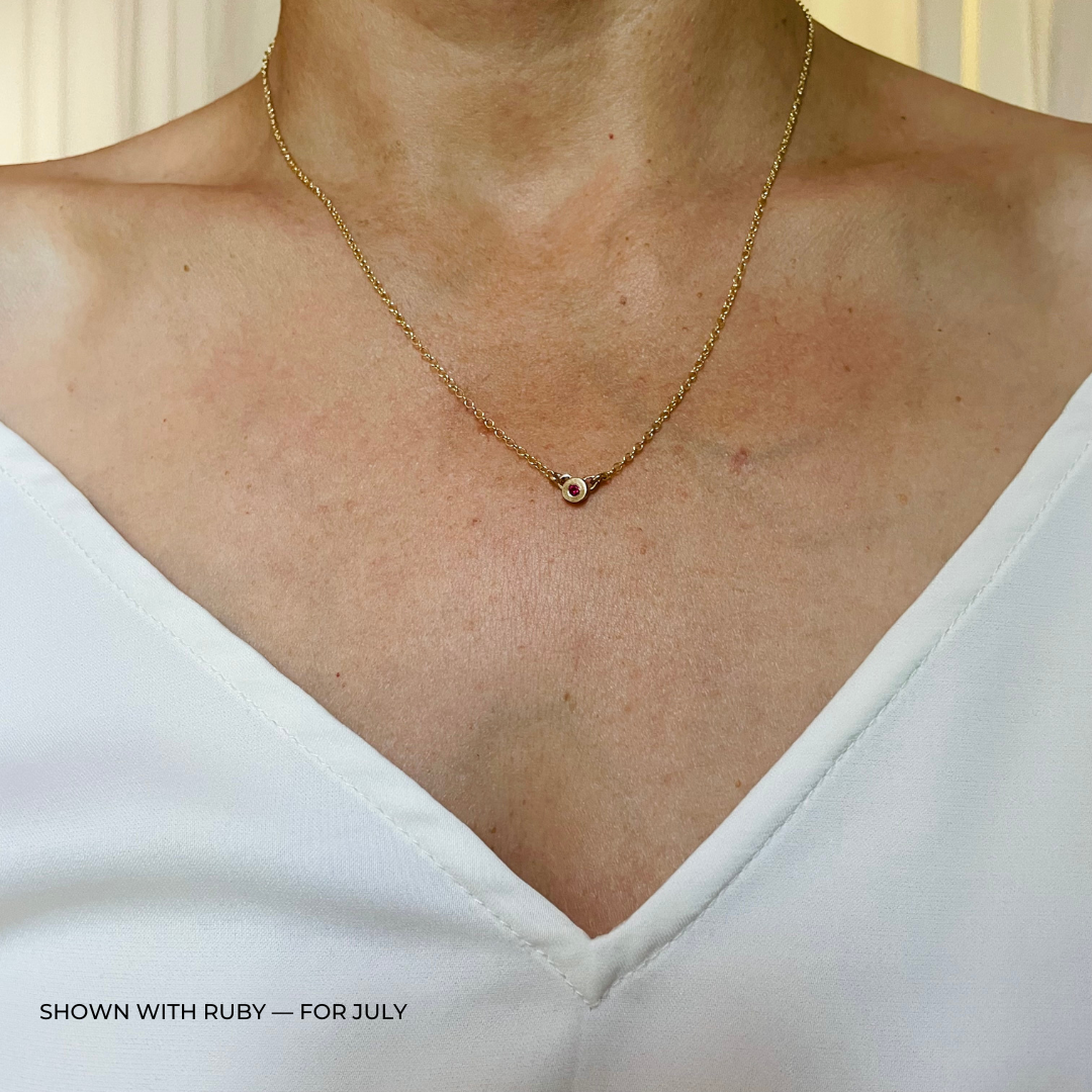 Handmade Bronze Birthstone Necklace with Ruby on Person Wearing a White Top