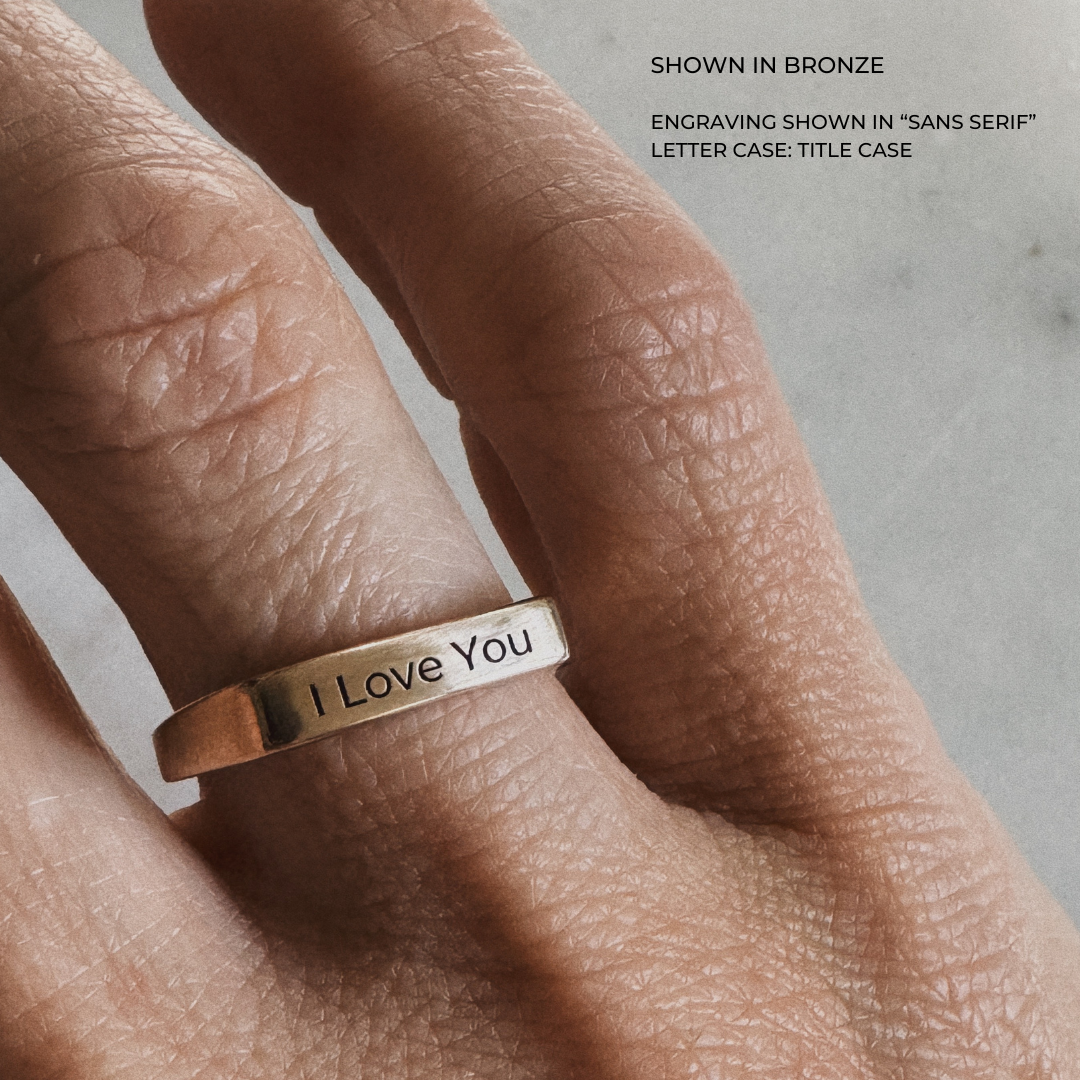 A custom engraved signet ring in a brushed bronze finish, featuring the words "I Love You" in title case sans serif lettering.