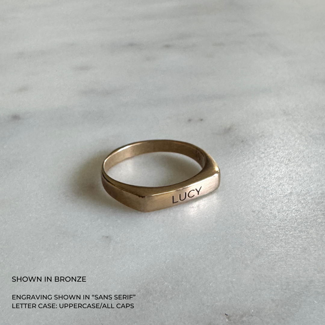 A custom engraved signet ring in a brushed bronze finish, featuring the name &