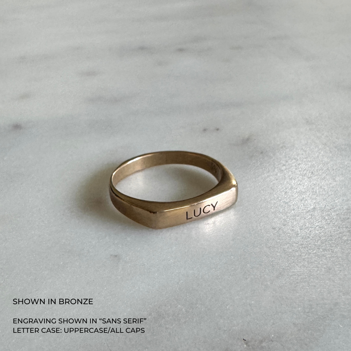 A custom engraved signet ring in a brushed bronze finish, featuring the name &