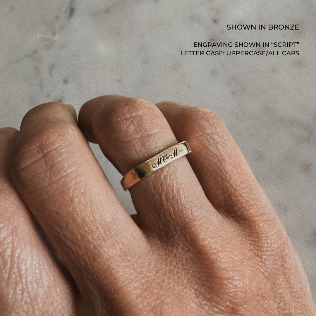 A custom engraved signet ring in a brushed bronze finish, featuring the name &