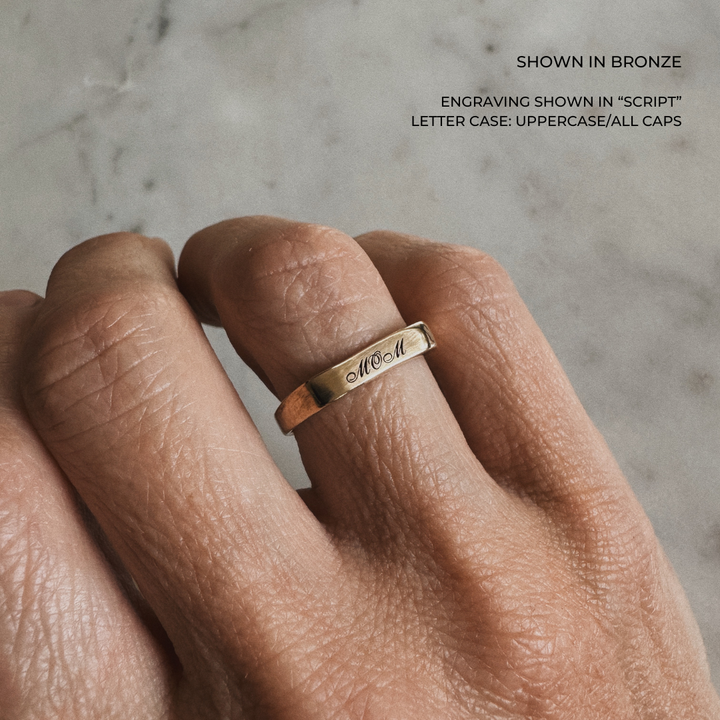 A custom engraved signet ring in a brushed bronze finish, featuring the name &