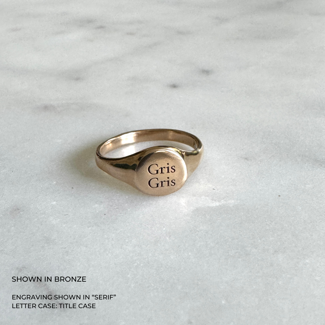 A round, bronze signet-style ring with the engraved text &