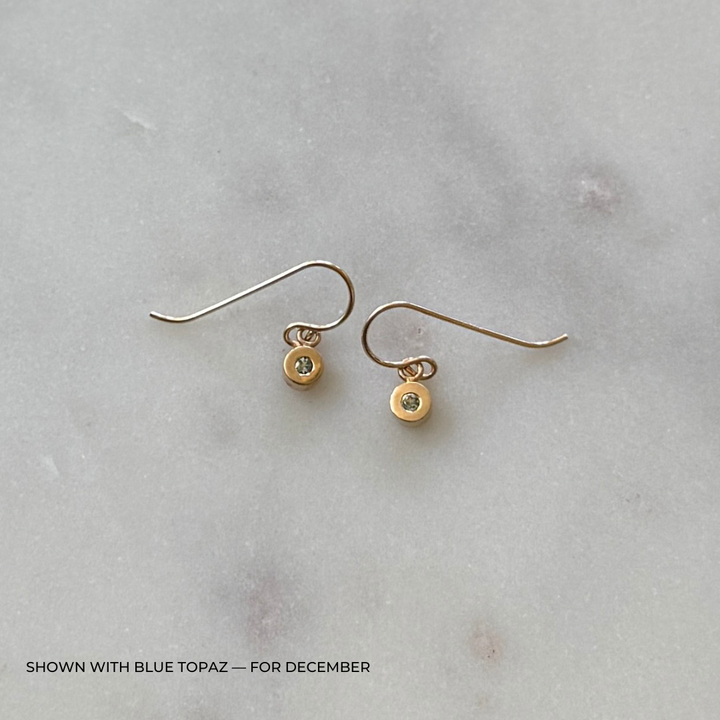 Bronze grace earrings with blue topaz gemstones on a light gray surface