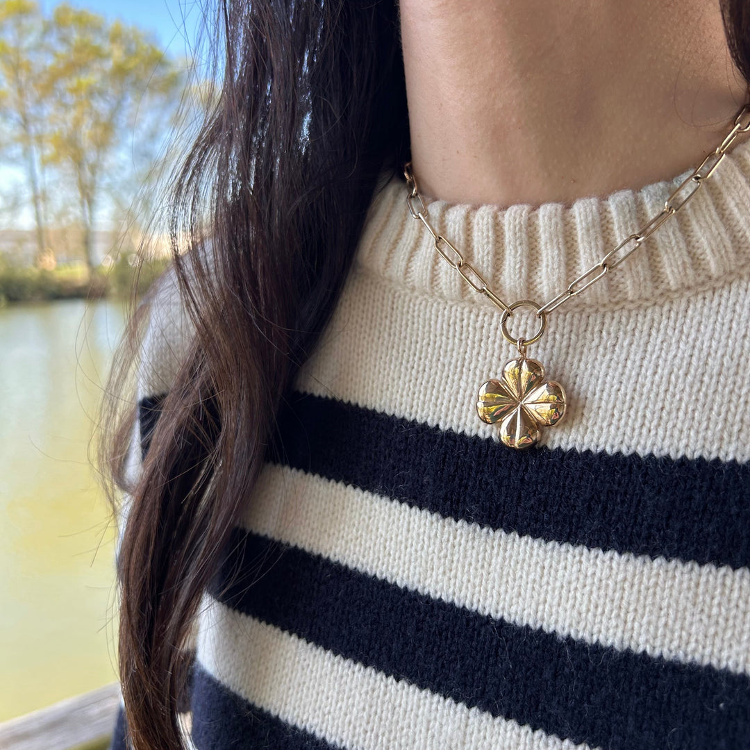 Person wearing a gold necklace with a clover pendant outdoors