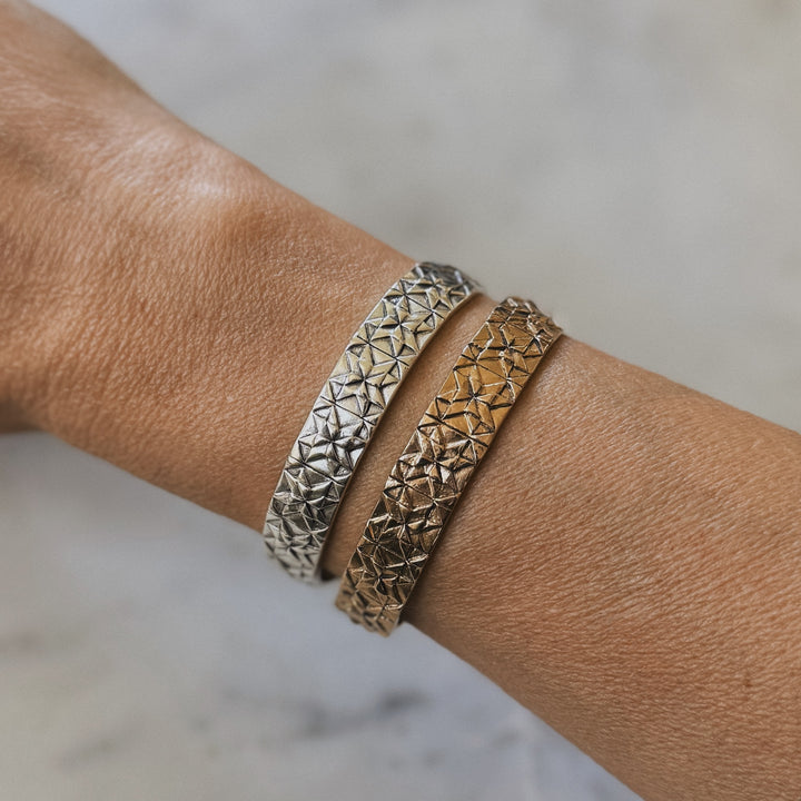 Person wears handmade quilt square bracelets in bronze and silver by MIMOSA Handcrafted