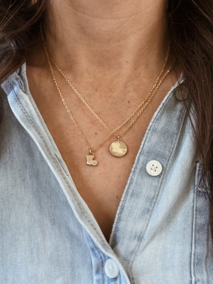 Woman Wears the MIMOSA Handcrafted Louisiana Burst and Louisiana State Pendants in Bronze