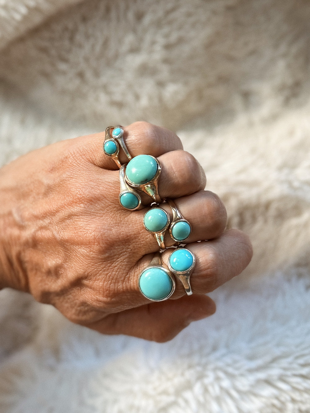 Hand Wearing Multiple Turquoise Gemstone Rings on a textured beige background