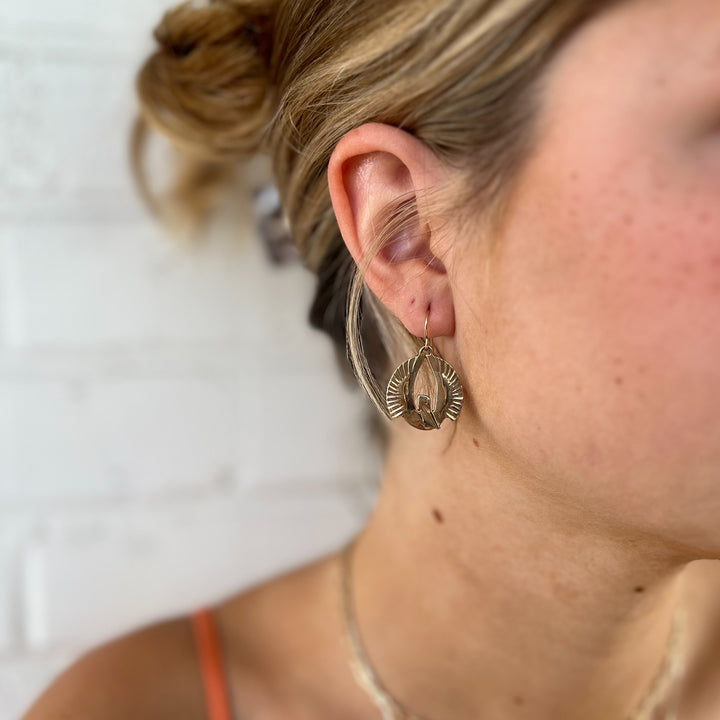 Woman Wears MIMOSA Handcrafted Small Pelican Rising Earrings in Bronze.