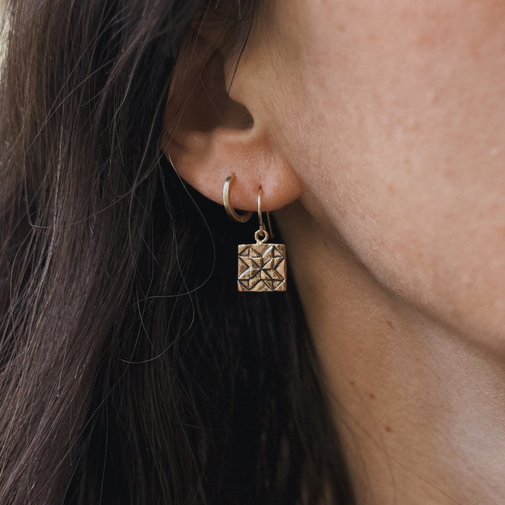 Person wears handmade quilt square earrings in bronze by MIMOSA Handcrafted