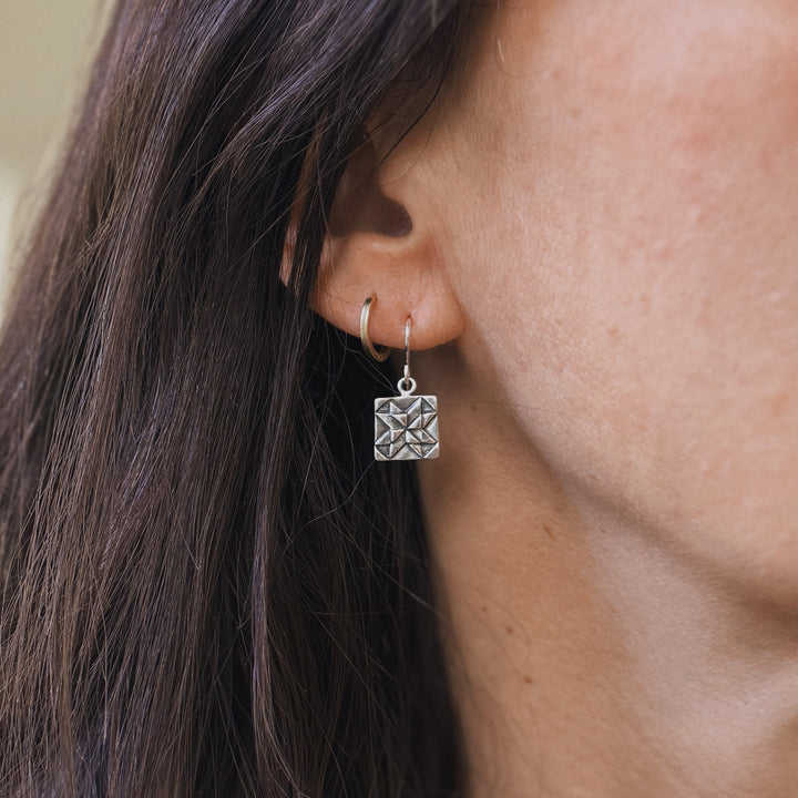 Person wears handmade quilt square earrings in sterling silver by MIMOSA Handcrafted