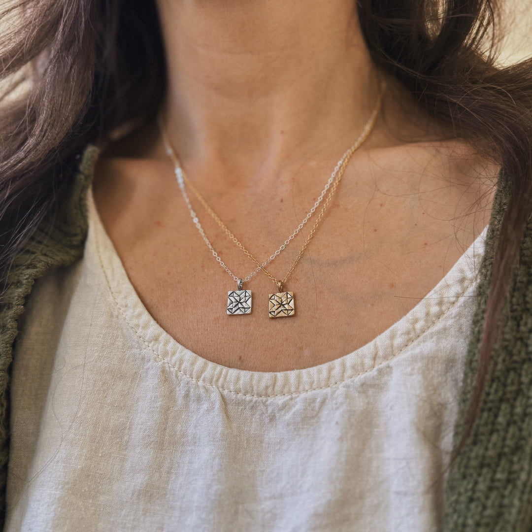 Person wears handmade quilt square necklaces in bronze and silver by MIMOSA Handcrafted