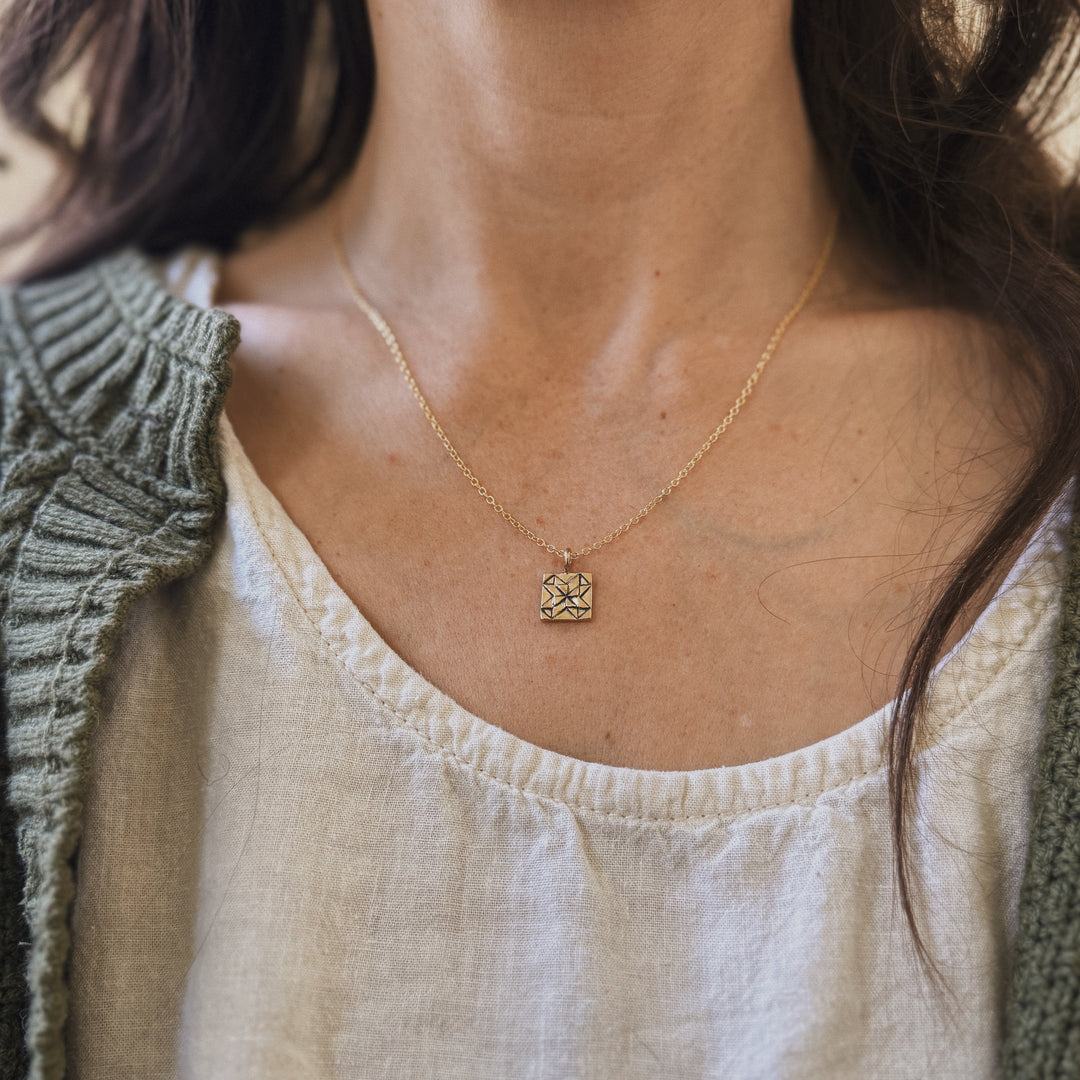 Person wears a handmade quilt square necklace in bronze by MIMOSA Handcrafted