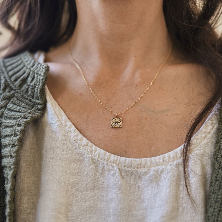 Person wears a handmade quilt square necklace in bronze by MIMOSA Handcrafted