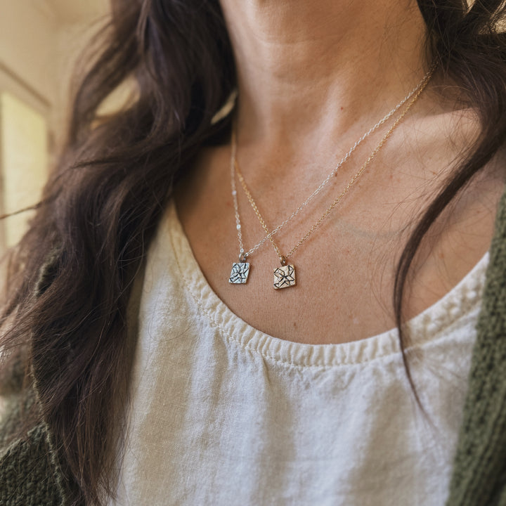 Person wears handmade quilt square necklaces in bronze and silver by MIMOSA Handcrafted