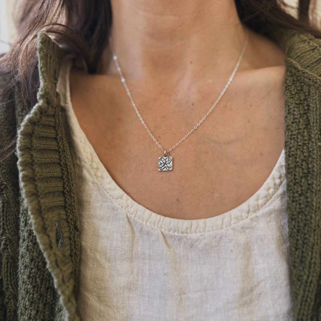Person wears a handmade quilt square necklace in silver by MIMOSA Handcrafted