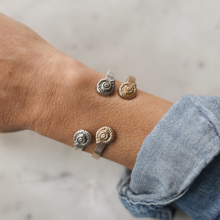 Close Up of a Wrist Wearing A Spiral Snail Shell Bracelet Design in Bronze and Silver