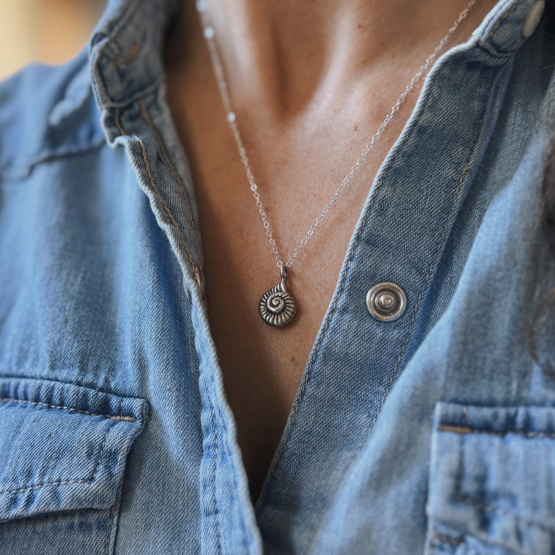 Close Up of a Person Wearing a Sterling Silver Snail Shell Necklace and Denim Shirt
