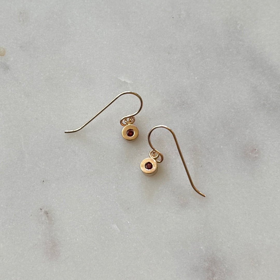 Bronze earrings with small round garnet gemstones on a light gray marble surface 