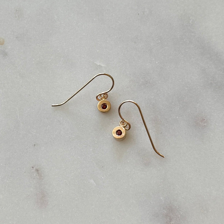 Bronze earrings with small round garnet gemstones on a light gray marble surface 