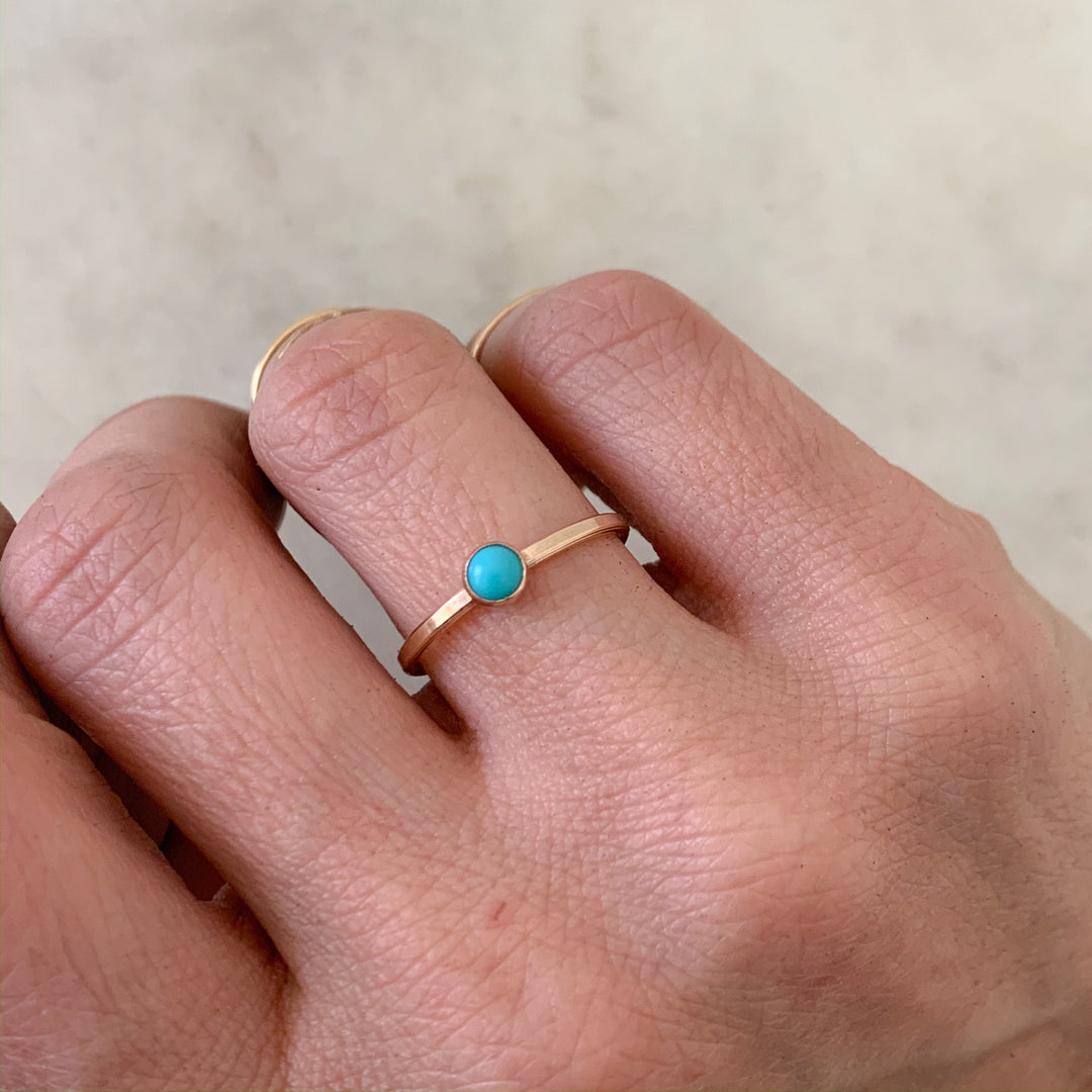 Hand Wearing Dainty Gold Ring with One Small Blue Turquoise Stone on ring finger